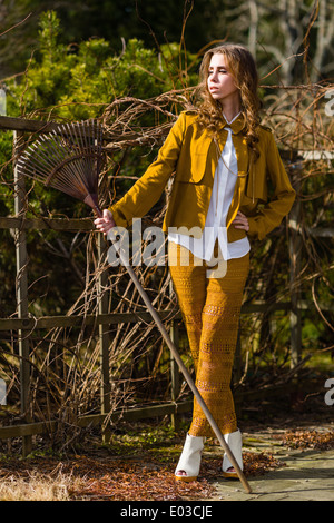 Beautiful fashionable woman and rake in the garden, springtime Stock Photo