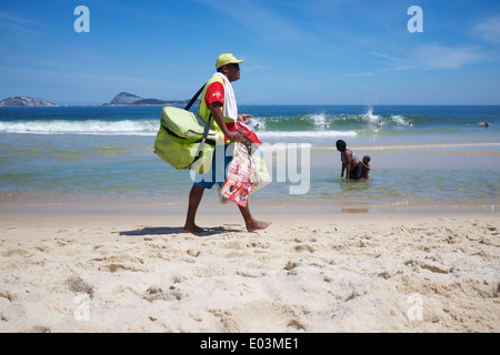 RIO DE JANEIRO, BRAZIL - FEBRUARY 23, 2014: Brazilian beach vendor selling ice cream walks along the shore of Ipanema Beach. Stock Photo