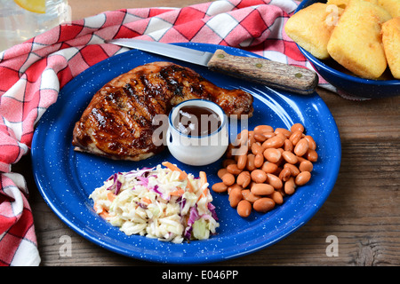 Closeup of a Barbecue chicken plate with cole slaw, pinto beans and corn bread. The meal is on a rustic wooden restaurant table Stock Photo