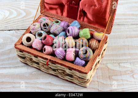High angle shot of a sewing box filled with thread. A variety of embroidery threads in a wicker basket on a rustic wooden table. Stock Photo