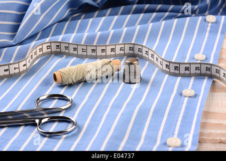 Closeup of a blue striped mens dress shirt ready for tailoring with scissors, thread, needle thimble and tape measure. Stock Photo