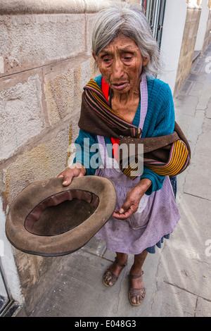 Bolivian woman beggar holding an empty hat out for money on a sidewalk in the central part of the city of Sucre. Stock Photo