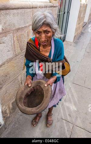 Bolivian woman beggar holding an empty hat out for money on a sidewalk in the central part of the city of Sucre. Stock Photo