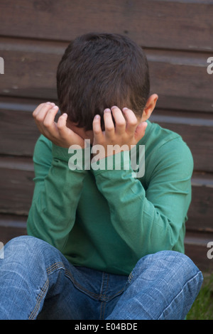 unhappy little boy sitting with hands covering face Stock Photo