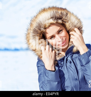 Closeup portrait of attractive young lady outdoors in wintertime, wearing stylish winter clothes, warm coat with furry hood Stock Photo