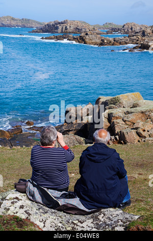 couple sitting on rock enjoying the views at Bryher, Isles of Scilly, Scillies, Cornwall in April Stock Photo