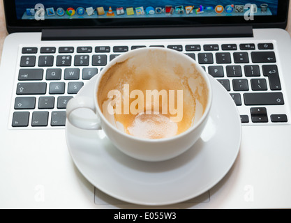 An empty cappuccino cup and saucer on a laptop Stock Photo