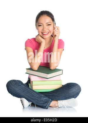 Full body Asian girl college student with pink shirt and jeans, stacks books, seated on floor isolated white background. Stock Photo