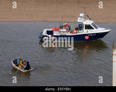 Two fishermen rowing dinghy out to fishing boat, Bude, Cornwall, UK Stock Photo