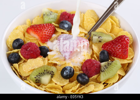 Milk pouring into fruit muesli with strawberries, raspberries, kiwi and blueberries Stock Photo