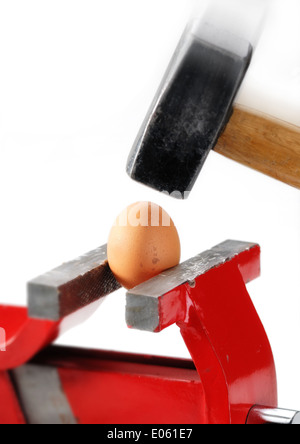 An egg gripped in the vise while a big and heavy hammer is almost hitting it Stock Photo