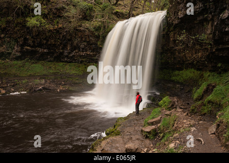 Female hiker stands near Sgwd yr Eira Waterfall - River Hepste, near Ystradfellte, Brecon Beacons national park, Wales Stock Photo