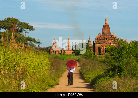 Woman with umbrella walking among ancient temple and pagoda in the jungle, Bagan, Myanmar Stock Photo