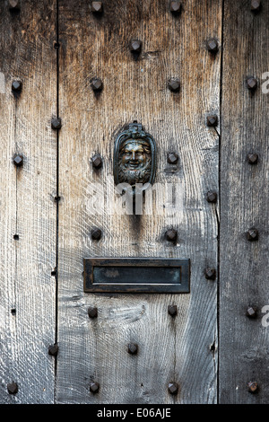 Old wrought iron face door knocker on an old wooden oak door in the Cotswolds, England Stock Photo