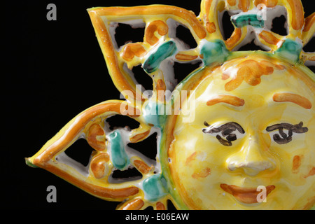 Italian ceramic ornament, in the form of a sun with a smiling face, on a black background. Isolated on black. Sicily, Italy. Stock Photo