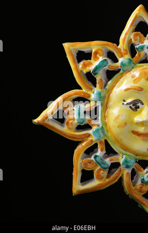 Italian ceramic ornament, in the form of a sun with a smiling face, on a black background. Isolated on black. Sicily, Italy. Stock Photo