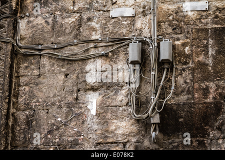 messy telephone or electricity cables hanged on a weathered wall Stock Photo