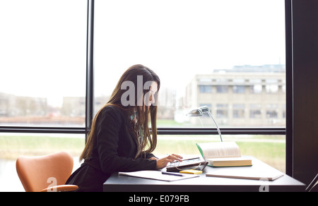 Young caucasian woman taking notes from digital tablet for her study. Female student sitting at table with books and tablet. Stock Photo