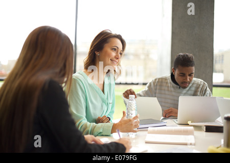 Group of students studying in library in college with woman looking away. Young people sitting at table with books. Stock Photo