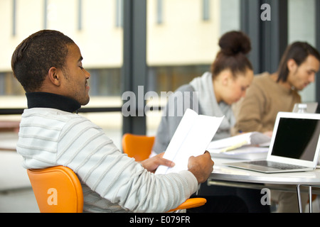 Young african american man reading notes with classmates studying in background in university library. Stock Photo