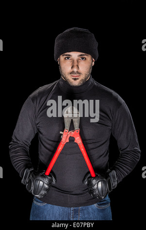 a burglar wearing black clothes holding huge wire cutters over black background Stock Photo