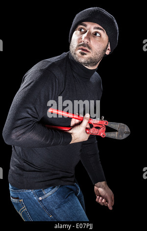 a burglar wearing black clothes holding huge wire cutters over black background Stock Photo