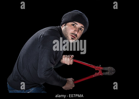 a burglar wearing black clothes holding huge wire cutters over black background Stock Photo