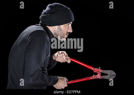 a burglar wearing black clothes holding huge wire cutters over black background Stock Photo