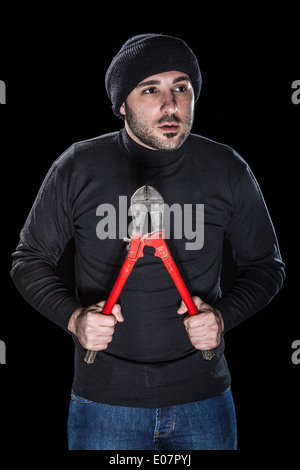 a burglar wearing black clothes holding huge wire cutters over black background Stock Photo