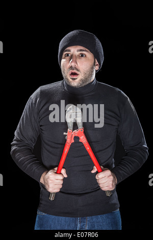 a burglar wearing black clothes holding huge wire cutters over black background Stock Photo