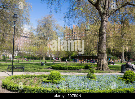 Russell Square in spring with people sitting, walking, relaxing with flowers in foreground Bloomsbury London England UK Stock Photo