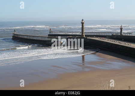 Breakwaters at the end of Whitby harbour mouth with lighthouse reflected in wet sand of beach Stock Photo