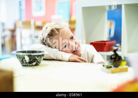 Smiling boy leaning on table in art class at kindergarten Stock Photo