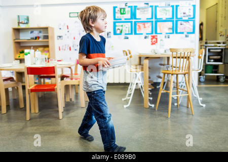 Elementary boy carrying plates in kindergarten Stock Photo