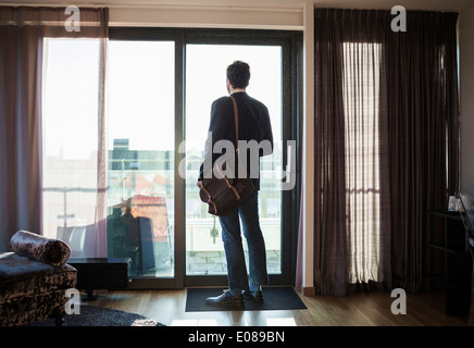 Rear view of businessman looking through window in hotel room Stock Photo