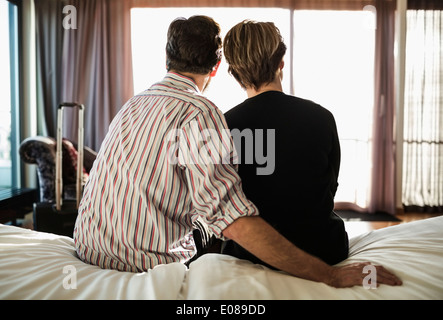 Rear view of business couple sitting on bed in hotel room Stock Photo