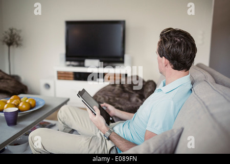 Side view of man with digital tablet sitting on sofa at home Stock Photo