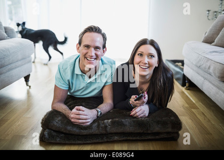 Happy couple watching TV while lying on floor in living room Stock Photo