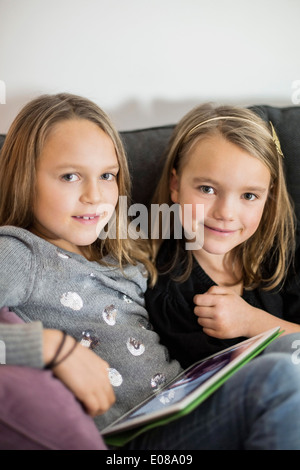 Portrait of sisters with digital tablet relaxing on sofa Stock Photo