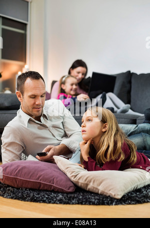 Father and daughter watching TV on floor with family in background Stock Photo