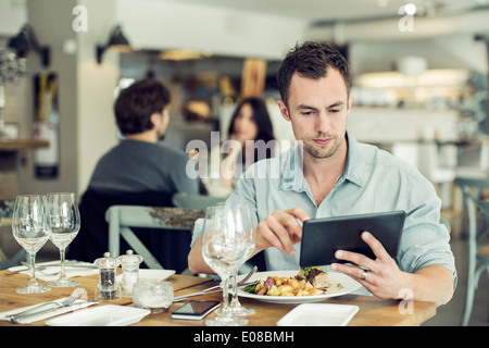 Mid adult businessman using digital tablet while having lunch at table in restaurant Stock Photo