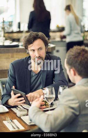 Mature businessman discussing over digital tablet with colleague at restaurant table Stock Photo