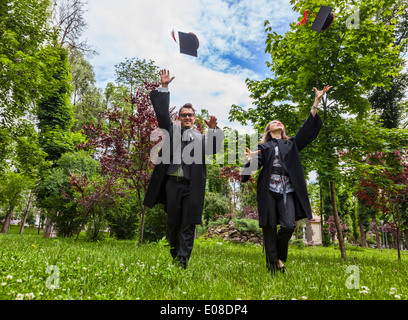 Happy couple in the graduation day running in a park and throwing their hats up. Stock Photo