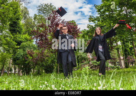 Happy couple in the graduation day running in a park and throwing their hats up. Stock Photo