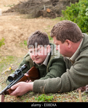 A young boy with an air rifle being coached in target shooting by his father Stock Photo