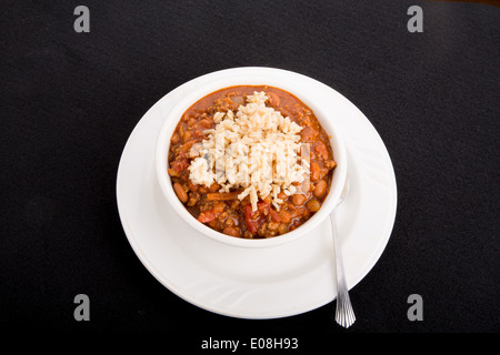 A white bowl of chili con carne with beans served over rice on a black background Stock Photo