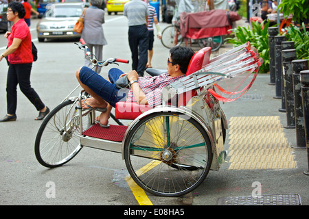 Sleeping on the Job, Man sleeps on duty in his cycle rickshaw, Albert Street, Singapore. Stock Photo