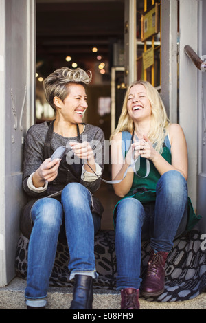 Happy female fashion designers sitting at studio doorway Stock Photo
