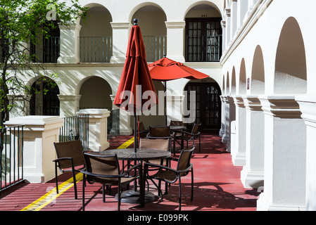 Tables and chairs under red umbrellas along an arched colonnade. Stock Photo
