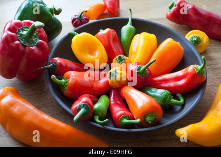 A mix of sweet and hot chilli peppers in a bowl and on a kitchen chopping board Stock Photo